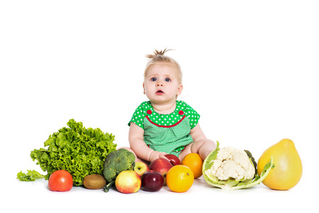Cute baby girl sitting surrounded by fruits and vegetables, isolated over white background. The concept of healthy food and happy lifeの写真素材