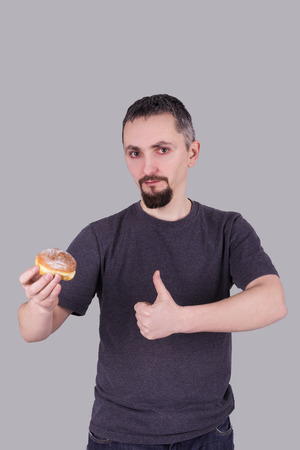Handsome man holds a bun in his hand and shows thumb up, isolated over gray backgroundの写真素材