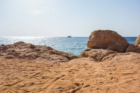 landscape picture background of a beach with sand mounds, stones cliff, blue sea with waves and sky