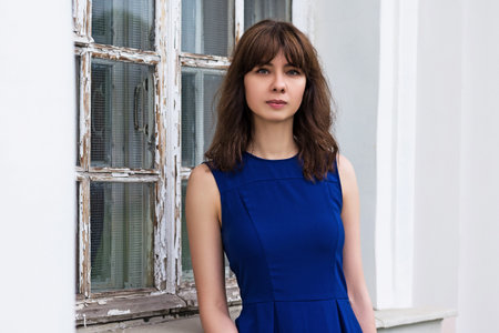 beautiful girl with asian appearance stands near the old white window and looks into the camera