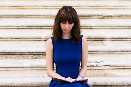 beautiful young girl in blue dress sitting on the steps and reading a book