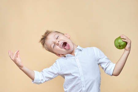 ? ute disheveled boy indulges and grimaces holding a pear in his hands.の写真素材