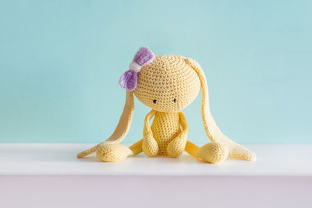 Soft toy knitted hare. Sitting yellow sad plush hare with a violet bow. Amigurumi.の写真素材