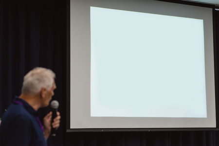 A big white screen without text. A conference concept. A speaker with a microphone is standing and...