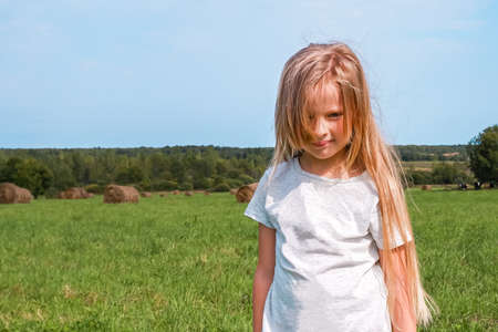Cute girl sitting on a hay roll in summer field. Childhood conceptの写真素材