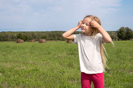 Cute girl sitting on a hay roll in summer field. Childhood conceptの写真素材
