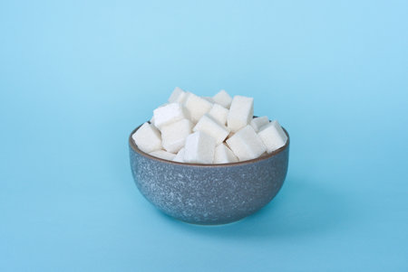 Refined sugar cubes in ceramic bowl on blue backgroundの写真素材