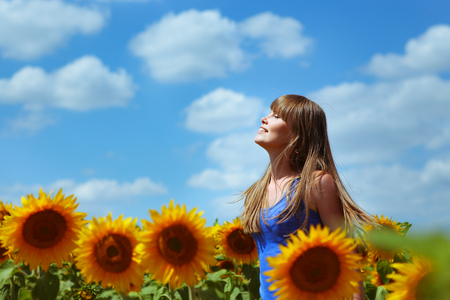 Happy young woman dreams before a beautiful sky and sunflowersの写真素材