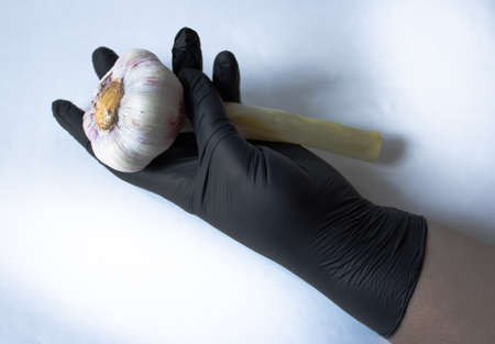 Female hands close-up in black latex gloves holding garlic. The photo can be used for articles as protection against covid-19, flu and other colds.の写真素材