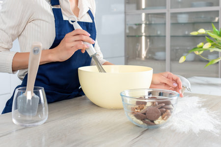 Female baker in blue apron mixing batter in big bowl. Process of making a pie or muffins