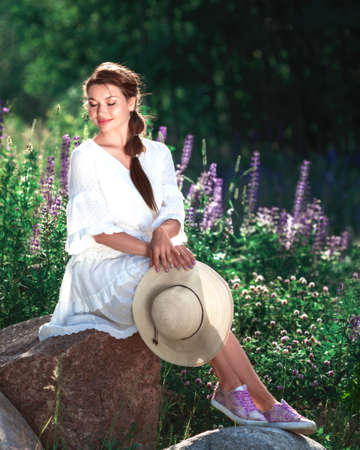 Portrait of young beautiful woman in white dress sitting at summer natureの写真素材
