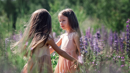 Portrait of twins sisters with long hair dancing together holding hands at grass and flowers.の写真素材
