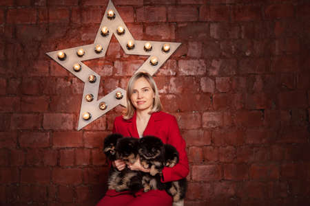 Smiling pretty business woman in red jacket holding cute puppies of pomeranian spitz breed dog. Owner or breeder with litter of puppies.の写真素材