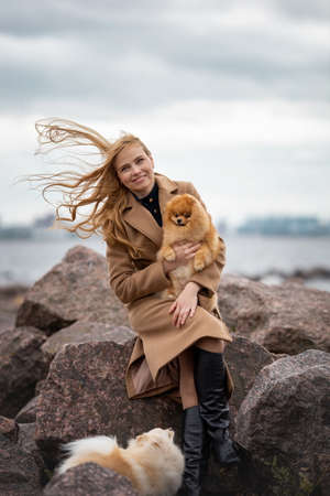Cute elegant woman is sitting with her dogs of pomeranian spitz breed near sea at nature.の写真素材