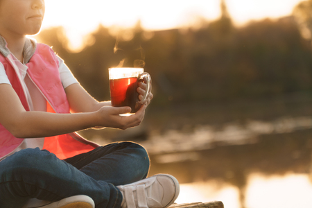 Smiling girl with cup of tea or coffee enjoying on summer shore of riverの写真素材
