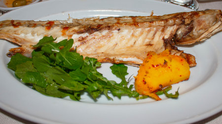 Half fried bass on plate with potatoes and arugula  Turkish cuisine
