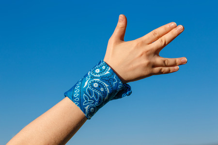 Hand with Vulcan salute on blue sky background and blue knotted bandanaの写真素材
