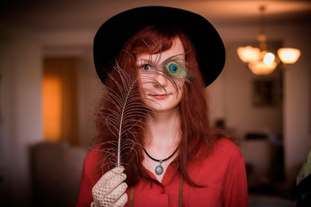 beautiful young model in a vintage costume (hat and gloves) with a peacock feather. photo toned...
