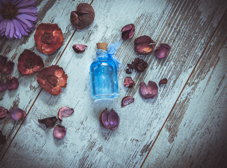 blue cologne in small bottle and dry flowers on old tree background. Photo toned and with vignette.の写真素材