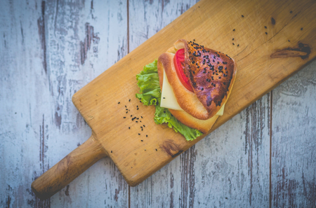 Sandwich with cheese, herbs and tomato on rough wooden boardの写真素材