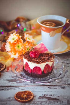 small strawberry cake dusted with grated chocolate on plate, flowers and cup of tea. photo with light effect, toned and with vignette.の写真素材