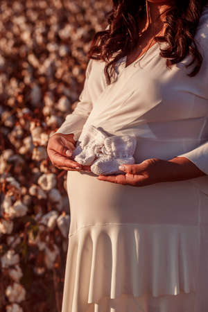 Man and pregnant woman holding bonnet for a newborn baby in a cotton fieldの写真素材