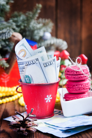 Twisted bills of dollars and euros in red christmas bucket, euro and pink macaroons. New year`s giftsの写真素材