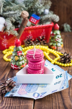 Pink macaroons and twenty euros with christmas decorations on woooden backgroundの写真素材