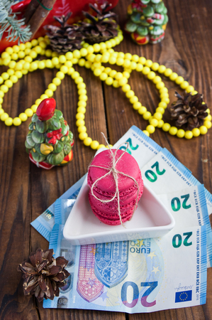 Pink macaroons and twenty euros with christmas decorations on woooden backgroundの写真素材