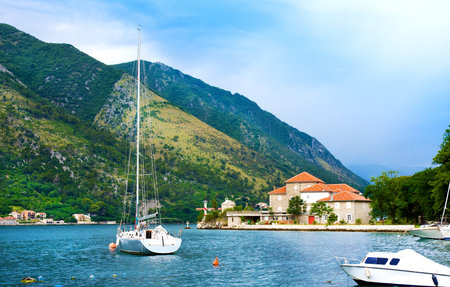 Yacht, house with red roof and boats near pier before storm, Kotor, Montenegro