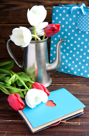 Bouquet of tulips, pot of coffee and gift bag, notepad with heart on wooden backgroundの写真素材