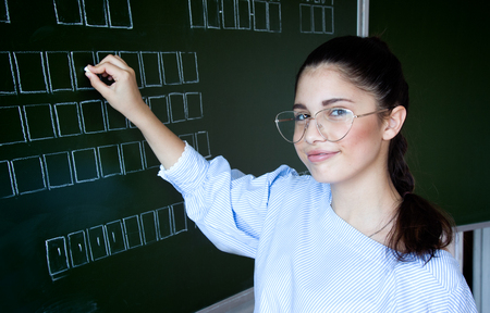 Girl in glasses stays near blackboard in classroomの写真素材