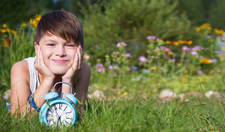 Boy with alarm clock lays in summer gardenの写真素材