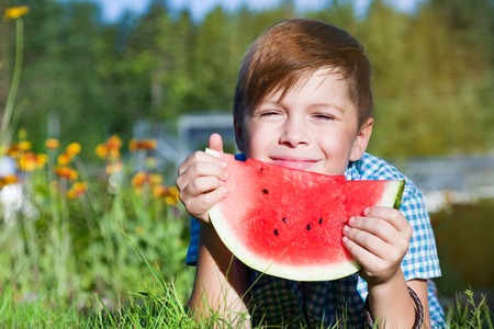 Funny boy eats watermelon outdoors in summer park, healthy foodの写真素材