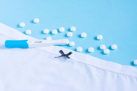 Female white panties with bow, birth control pills or vitamin and pregnancy test on blue background. Health care, contraception and planned pregnancyの写真素材