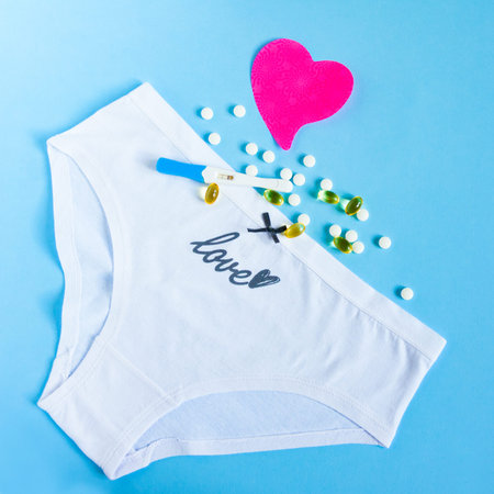 Female white panties with bow, birth control pills or vitamin, pink paper heart and positive...