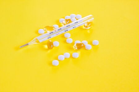 Glass mercury thermometer, white pills and capsules on yellowbackground. Fever heat, antipyretic tablets, cold. Medicine conceptの写真素材