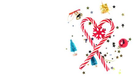 Heart shape made with candy canes on white background with new year decorations: toy trees. bell, snowflake, present, ball and confetti. Christmas mood. Winter Holidaysの写真素材