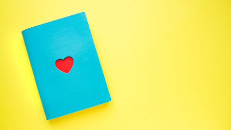 Blue notebook with red heart on yellow background.Flat lay. St. Valentin`s day. Book with love