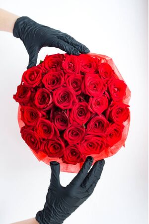Hands in black medical gloves with red roses in paper box. Contactless flower delivery during isolation during coronavirus pandemic.の写真素材