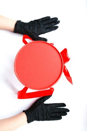Hands in black medical gloves and red gift box with copy space.Contactless delivery during isolation during coronavirus pandemic.の写真素材