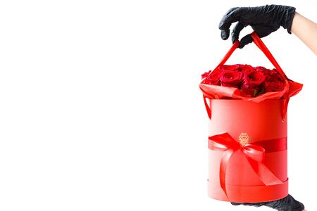 Hands in black medical gloves with red roses in paper box. Contactless flower delivery during isolation during coronavirus pandemic.の写真素材