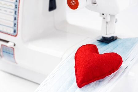 Red heart on mask face fabric. Health care and coronavirus protect with sew mask. Sewing medical masks to protect against coronavirus.Production of masks on sewing machine during quarantineの写真素材