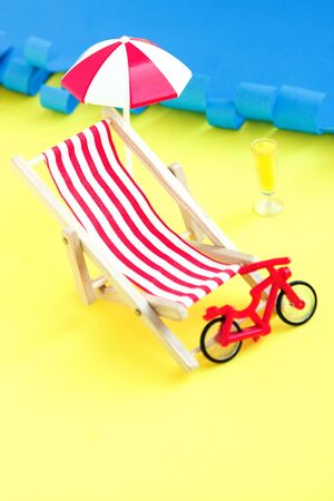 Red toy bicycle and beach deck chair and umbrella against sea. Summer rest. Vacations near seaの写真素材