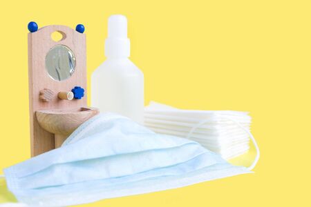 Wooden toy washbasin, medical protective mask and anti-bacterial disinfectants in white vials on yellow. Concept personal hygiene during pandemic coronavirus. Frequent and thorough hand washingの写真素材