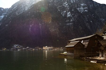 Halstatter lake in sun rays near traditional wooden boat houses and against mountains in famouse village Hallstatt, Salzkammergutの写真素材