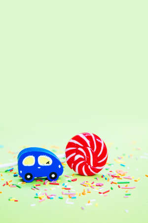 Toy wooden blue car and lolipop with confetti on green backgroundの写真素材