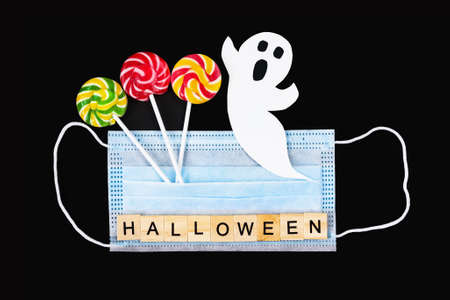 Cut out paper ghost, colorful lollipops, medical mask and word Halloween on black. Halloween background decor holiday conceptの写真素材