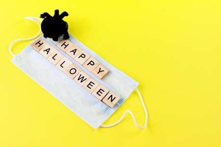 Black toy spider, medical mask and words Happy Halloween on yellow. Halloween background decor holiday conceptの写真素材