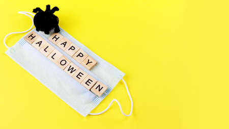 Black toy spider, medical mask and words Happy Halloween on yellow. Halloween background decor holiday concept. Copy space. Bannerの写真素材